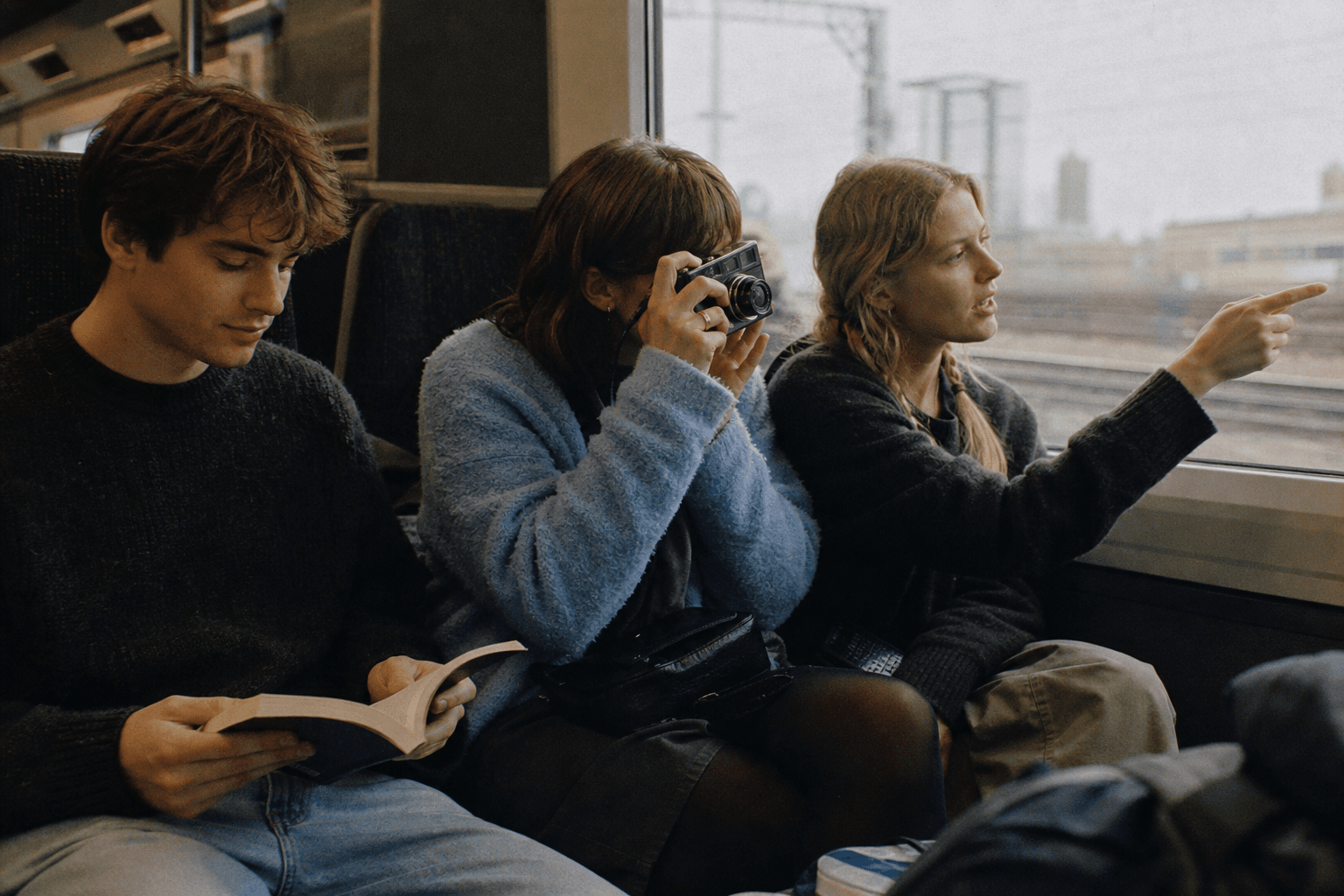 Three students reading and taking photographs on a train